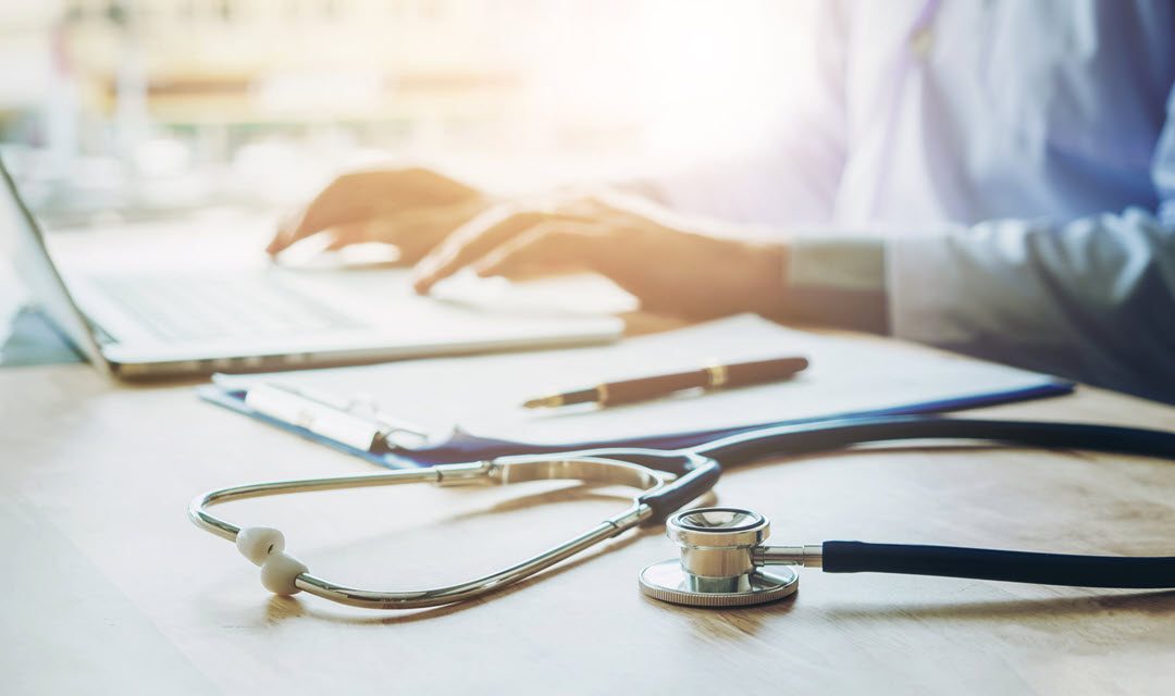 Person on a laptop with a stethoscope on his desk